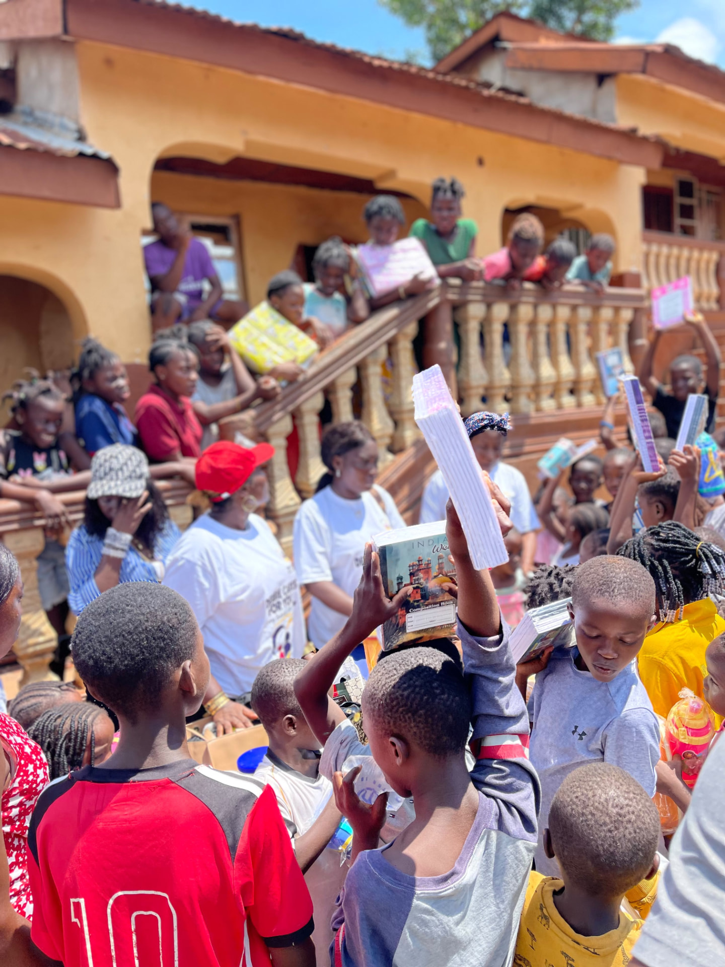 Children proudly hold up new exercise books outside a house as volunteers hand out supplies